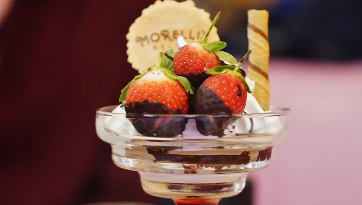 Chocolate-dipped strawberries in a clear glass bowl with a wafer cookie, shot with selective focus and warm studio lighting.