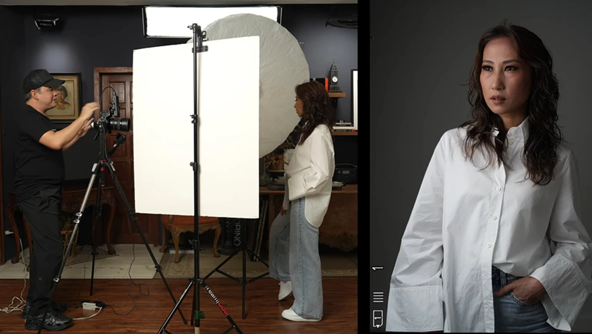 Professional portrait of a woman in white shirt against dark background, with behind-the-scenes studio setup visible on the left.