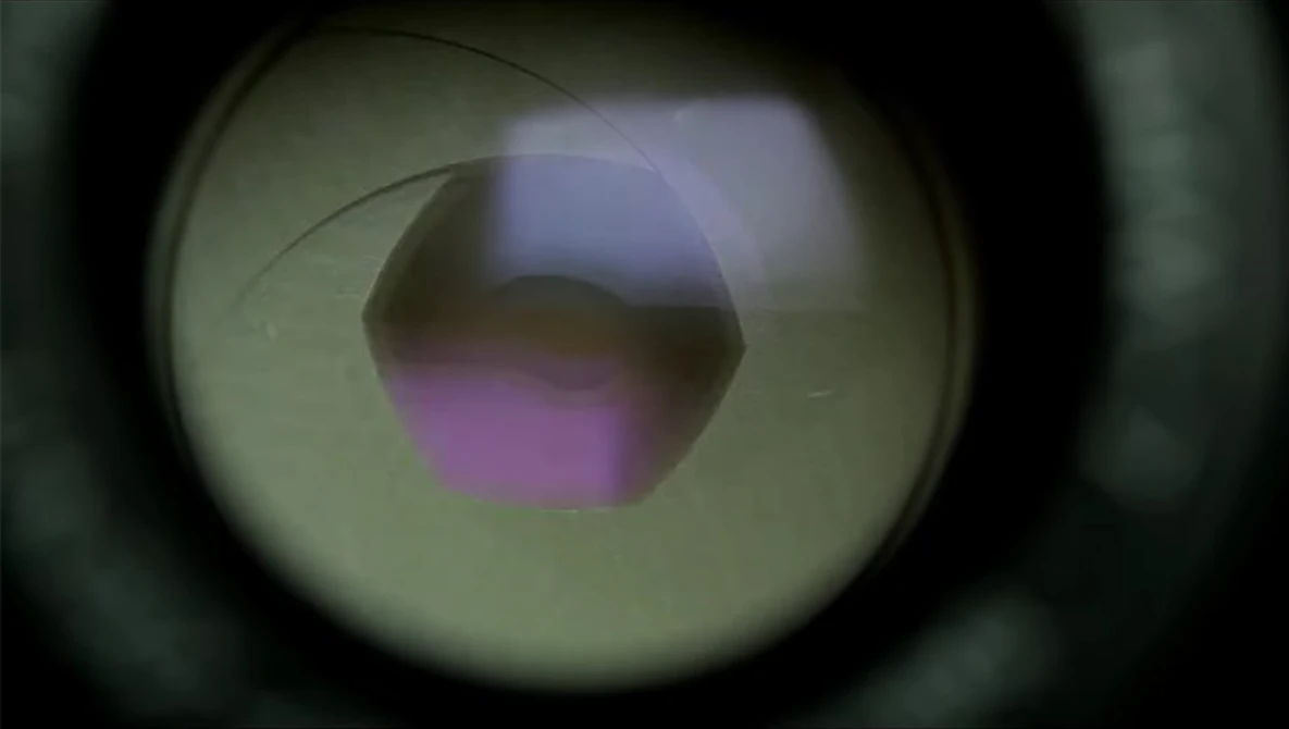 Close-up view through a camera lens showing a purple and blue aperture opening with light refraction.