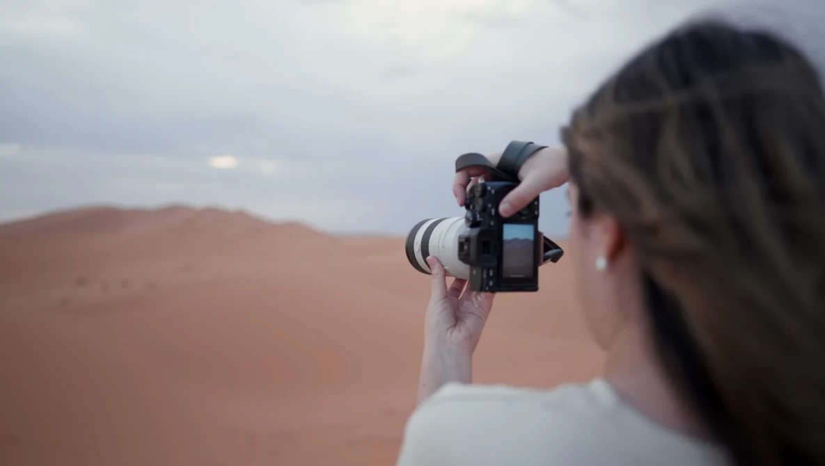 Photographer holding a mirrorless camera with telephoto lens while shooting in a desert landscape.