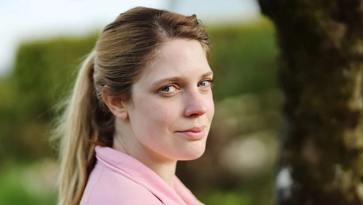 Woman in pink shirt looking over shoulder with soft natural outdoor lighting.
