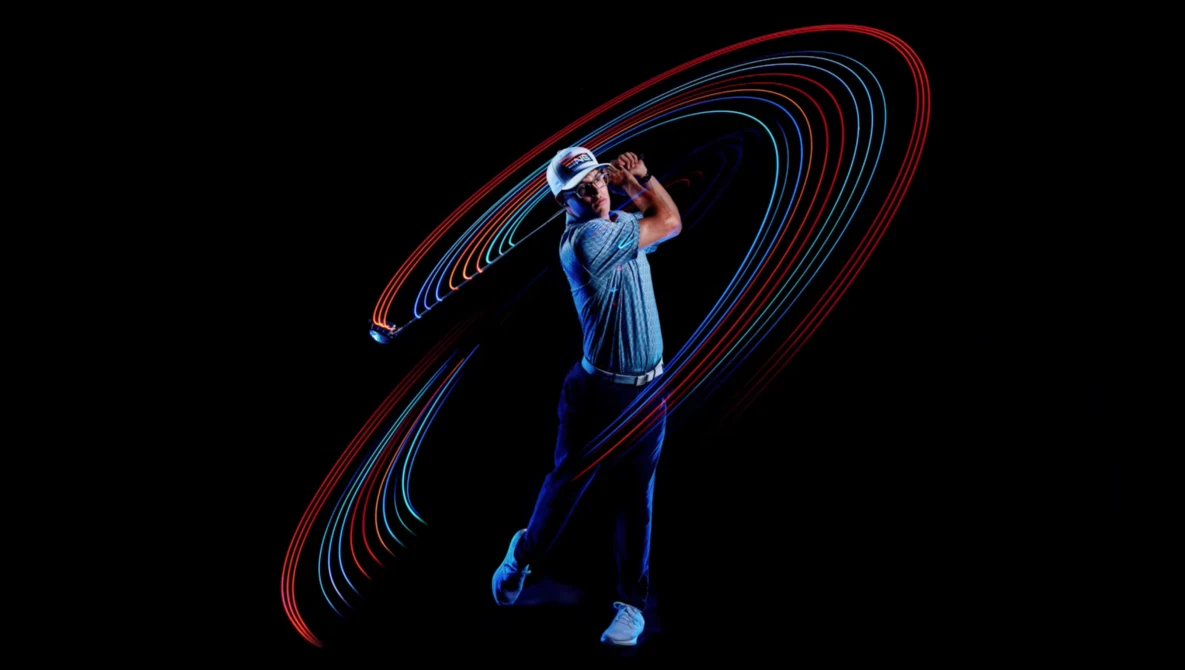 Golfer mid-swing photographed with light painting technique creating red and blue motion trails against black background.