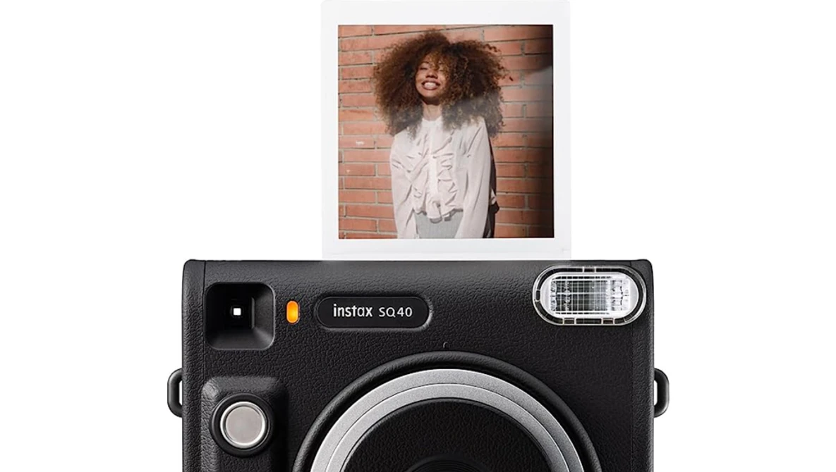 Instax SQ40 instant camera with sample portrait photo above showing smiling person against brick wall.