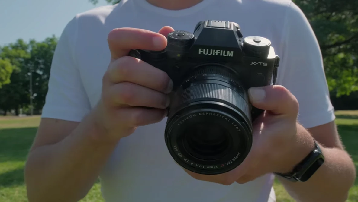Photographer holding a Fujifilm X-T5 mirrorless camera with attached lens outdoors.