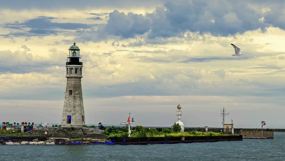 Historic stone lighthouse with multiple structures on a breakwater under dramatic cloudy skies.