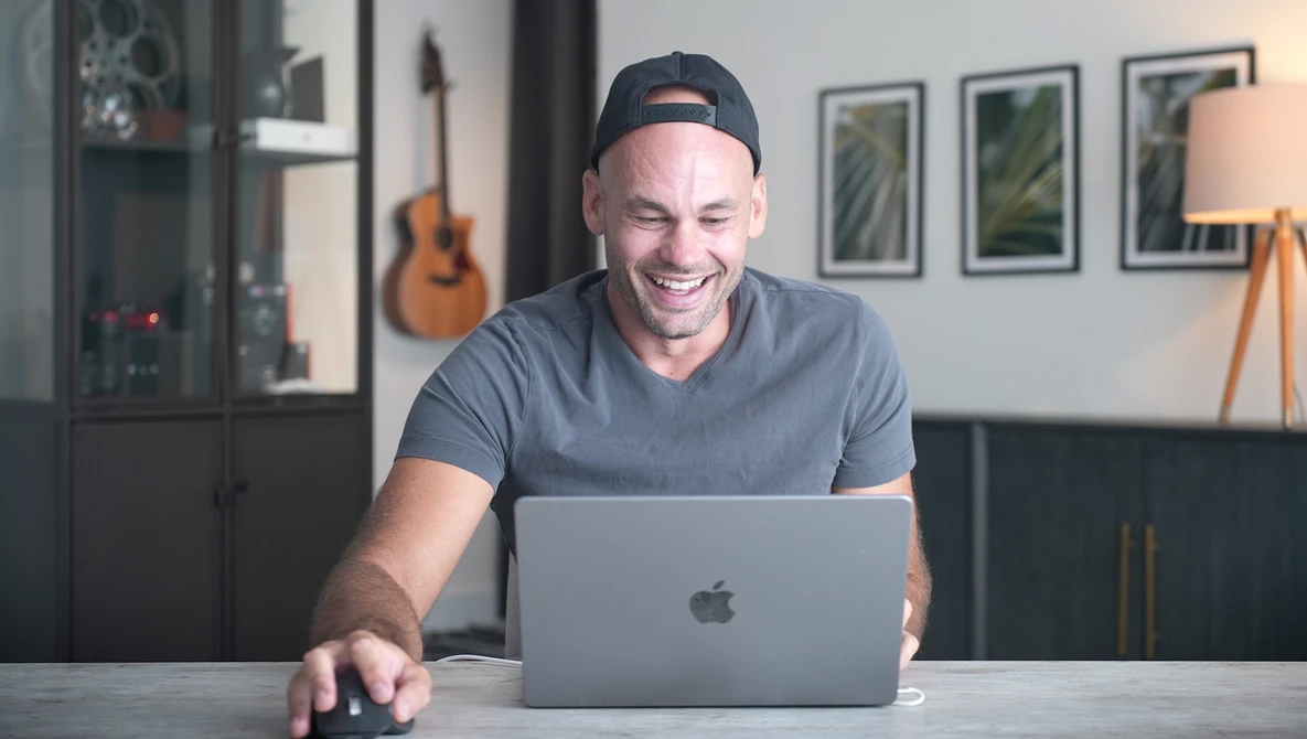 Man smiling at laptop while working at desk in modern home studio.