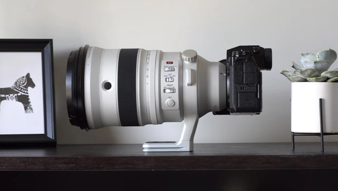 White telephoto lens mounted on black camera body, displayed horizontally on wooden shelf.