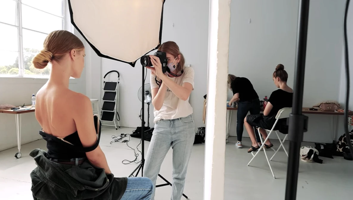 Photographer shooting a portrait of a model in a studio with professional lighting setup.