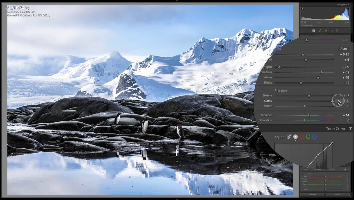 Snow-covered mountain peaks reflected in still water with dark volcanic rock in foreground.