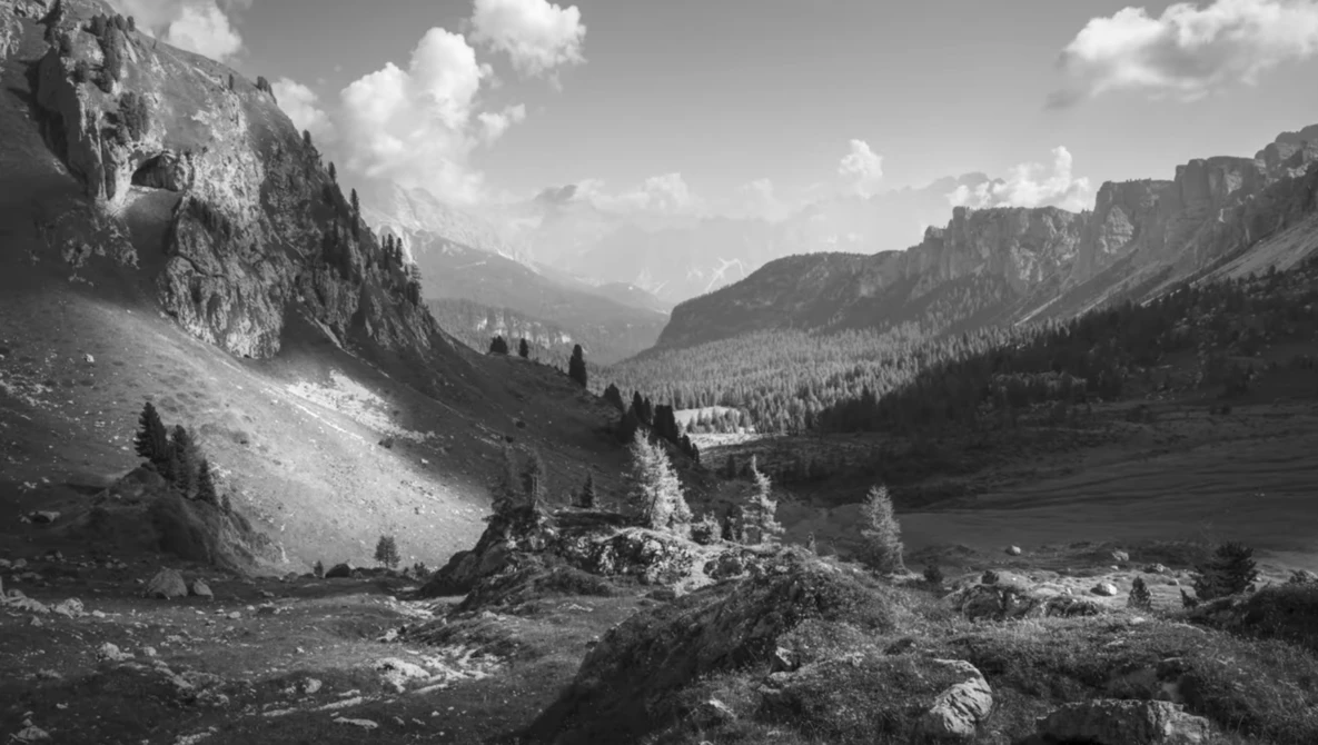 Alpine valley framed by steep rocky cliffs and forested slopes under cloudy sky.