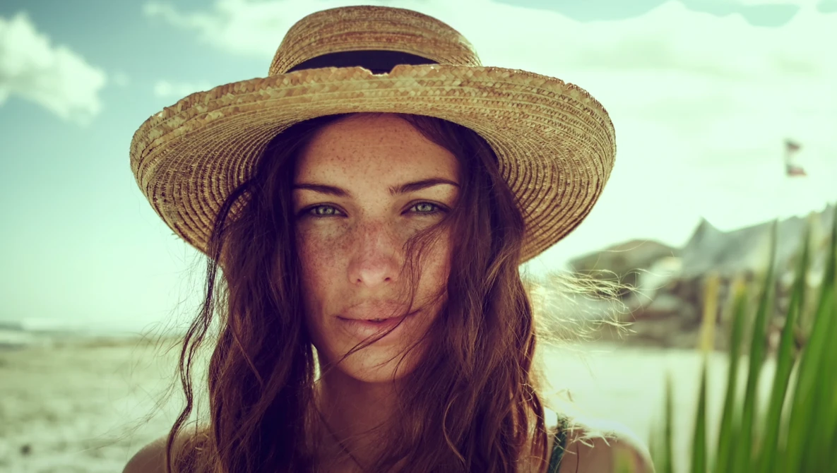 Woman wearing a straw hat looking directly at camera outdoors.