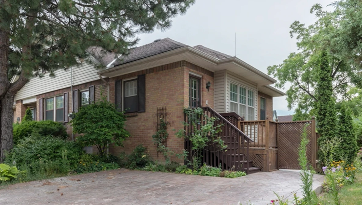 Brick residential home with ivy-covered entrance and wooden deck surrounded by mature trees.