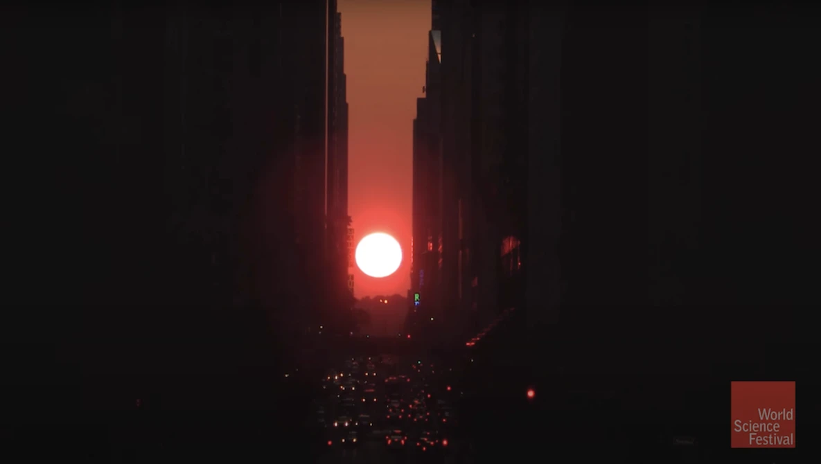 Bright red sun framed by tall buildings in a narrow urban canyon at dusk.