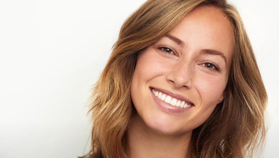 Woman with wavy brown hair smiling directly at camera against white background.