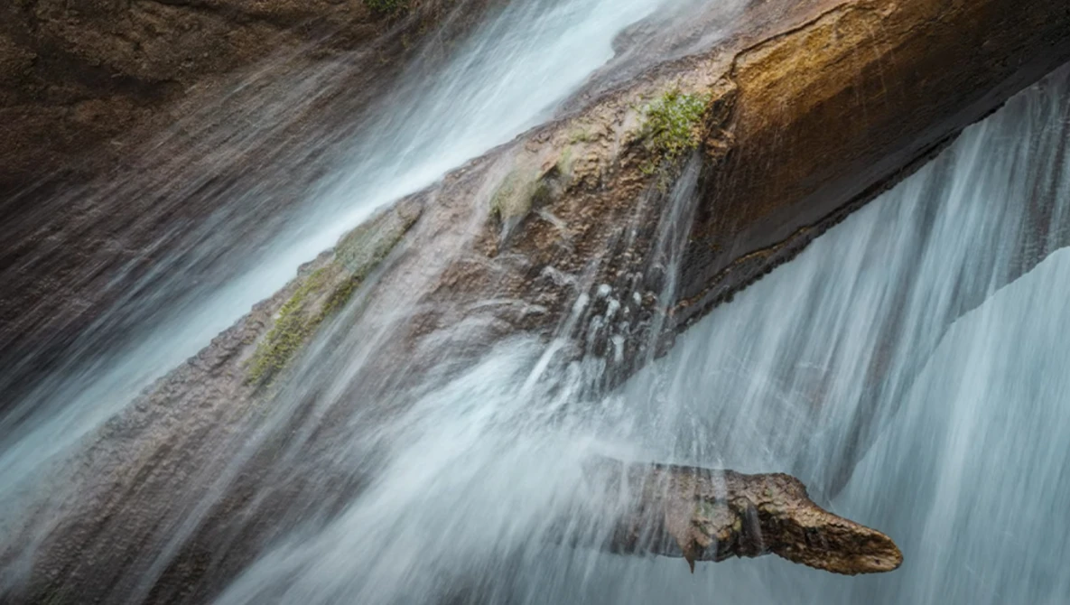 Flowing water cascades over layered rock formations with silky motion blur effect.