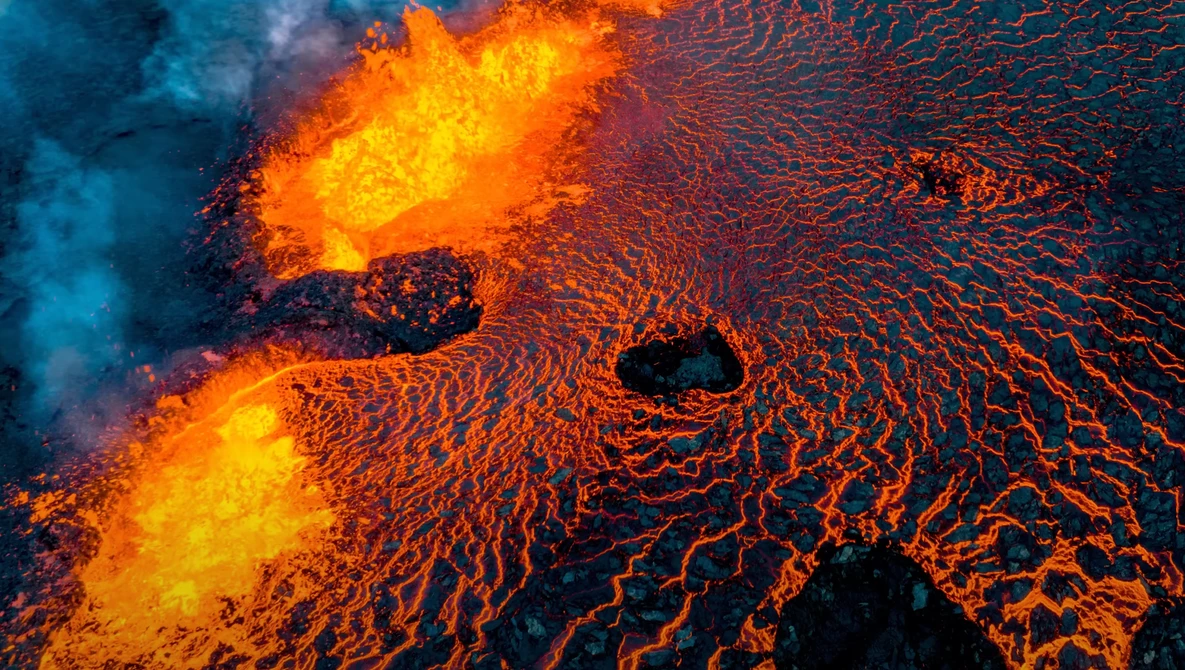 Aerial view of flowing lava with bright yellow-orange incandescent cores and darker solidifying edges creating intricate branching patterns.