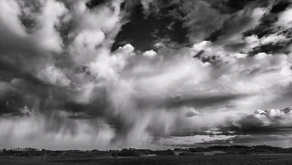 Dramatic black and white storm clouds with rain curtains over a flat landscape.