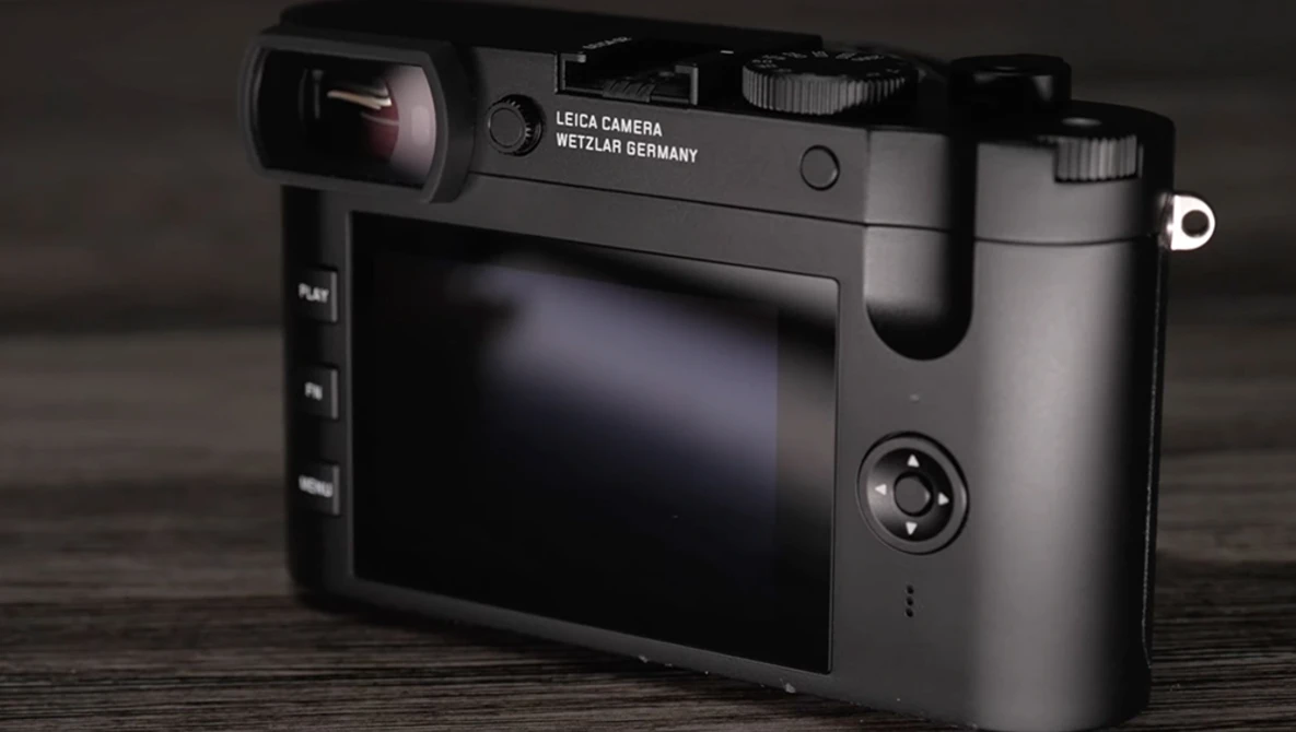 Leica camera with rear LCD screen displayed at three-quarter angle on wooden surface.