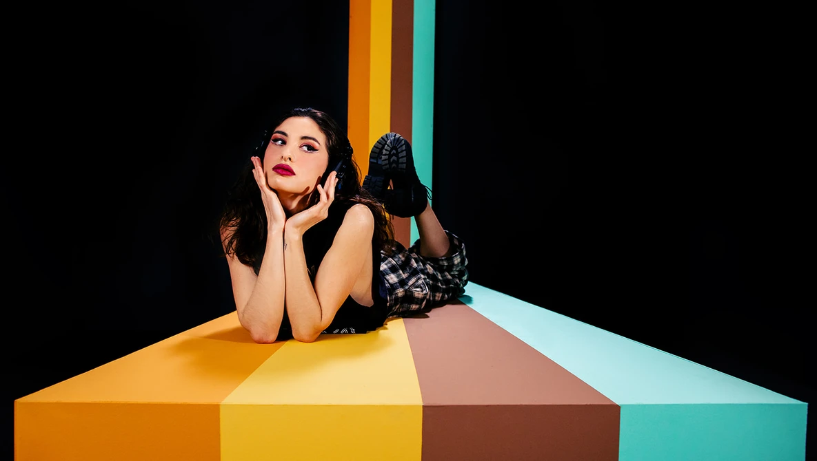 Woman resting her head on a colorful geometric surface against a black background.
