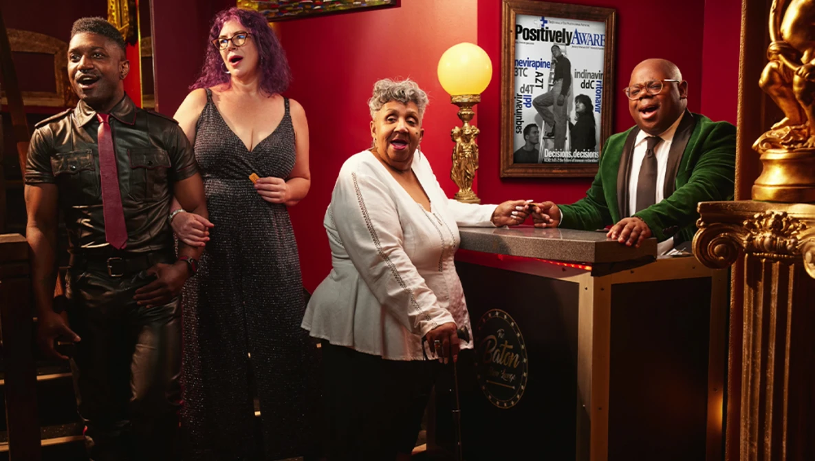 Four people in formal attire pose together in a warm-lit, burgundy-walled interior space decorated with gold accents.