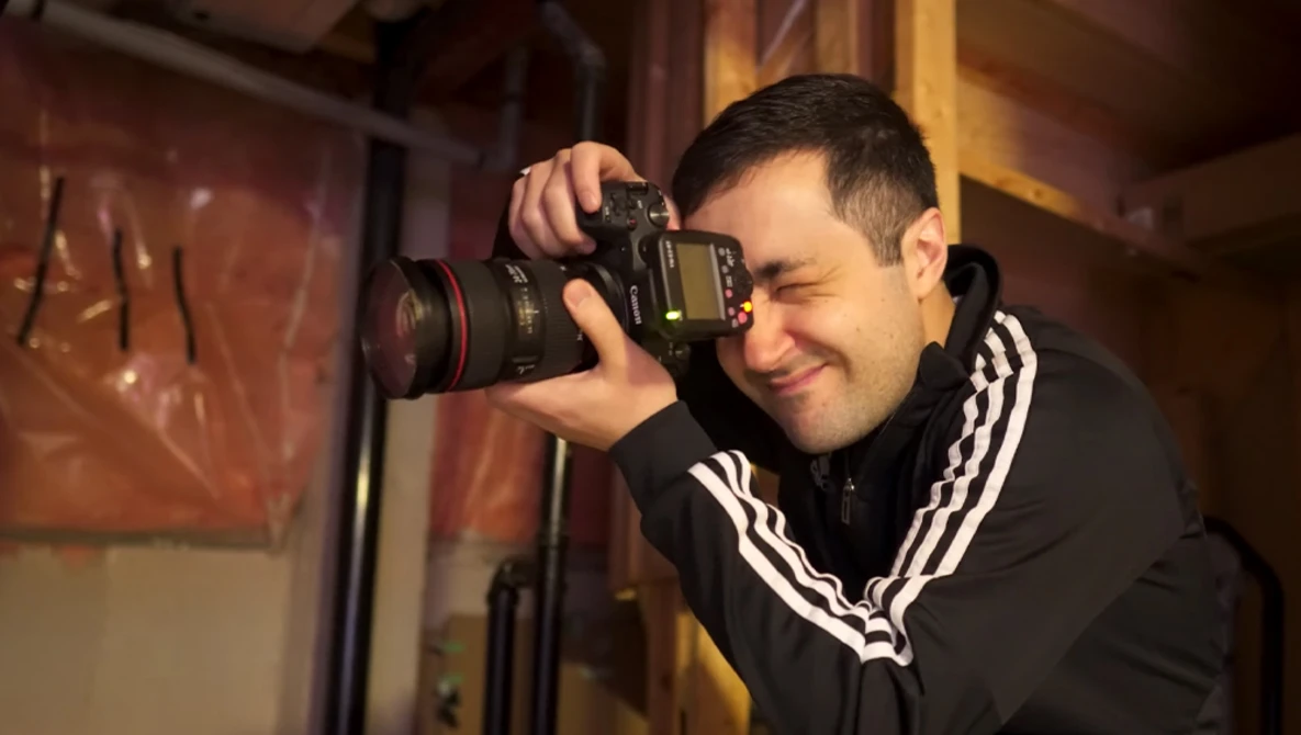 Photographer holding a DSLR camera with telephoto lens, smiling while composing a shot in warm indoor lighting.