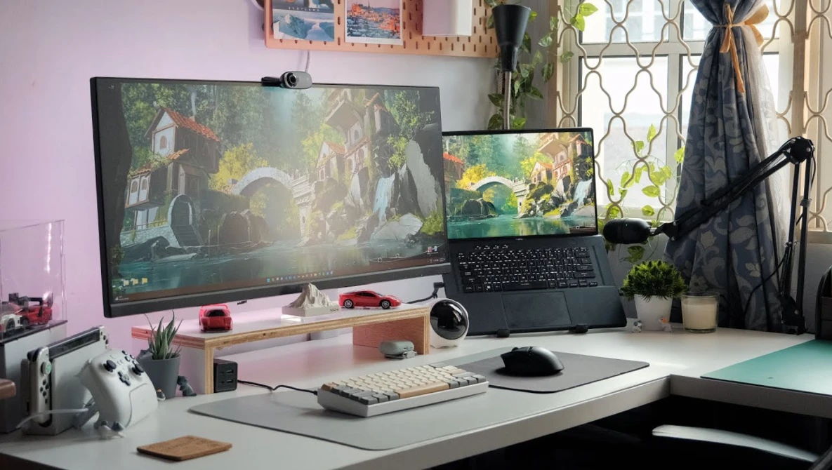 Dual-monitor creative workstation with laptop displaying landscape scene and desktop displaying forest environment.