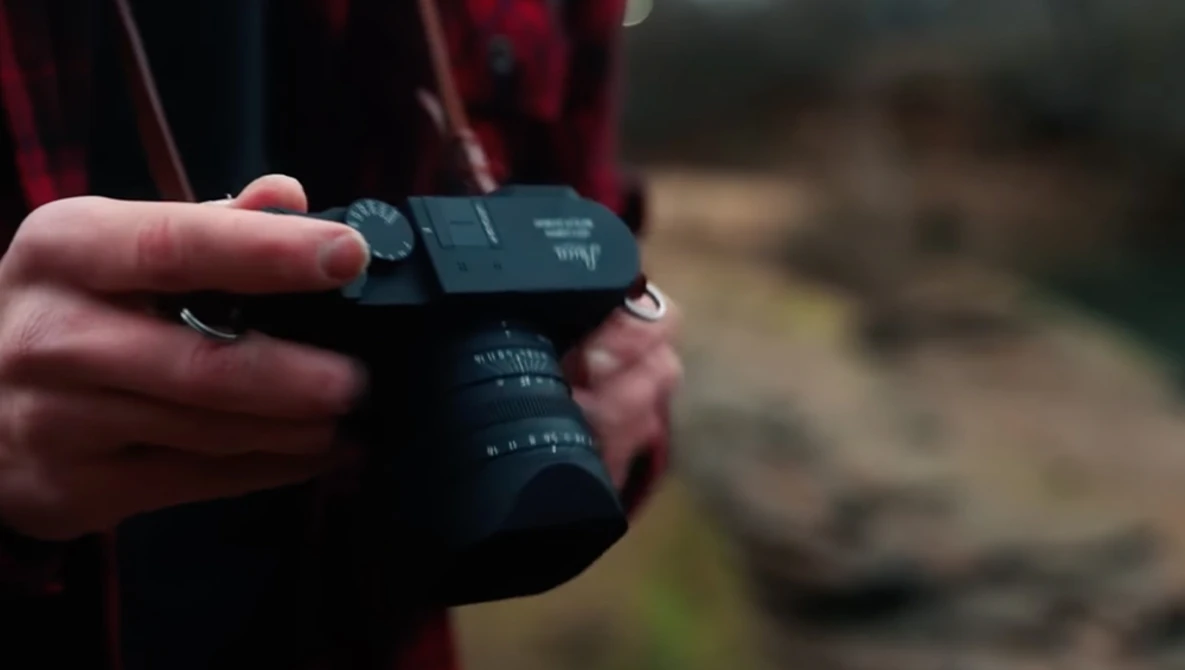 Photographer's hands holding a mirrorless camera with an articulating LCD screen in an outdoor setting.