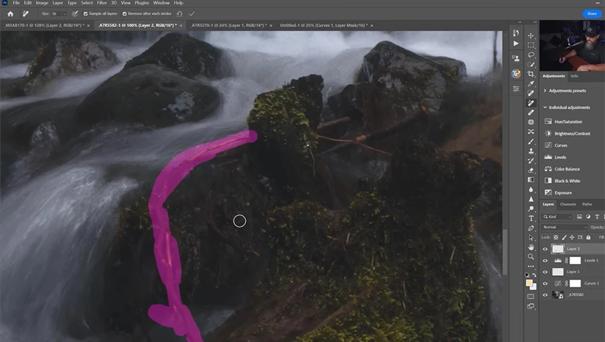 Screenshot of Photoshop editing interface with a landscape photograph of a flowing stream and mossy rocks, with a magenta curved selection tool visible.
