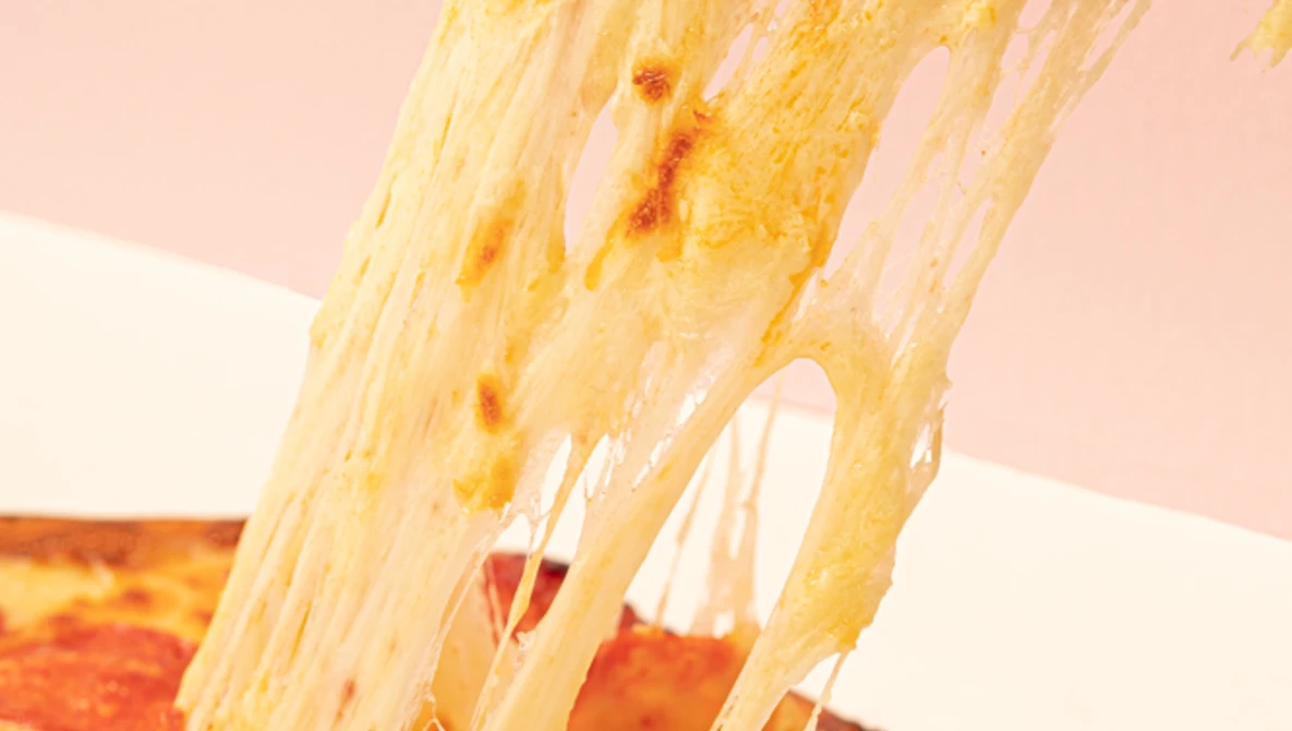 Melted cheese stretching from a pizza slice against a soft pink background.