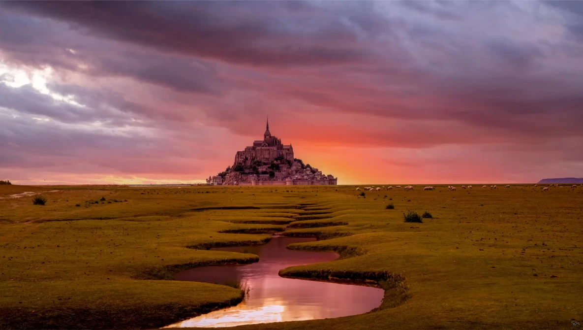 Medieval hilltop castle silhouetted against dramatic sunset sky with winding stream in foreground.