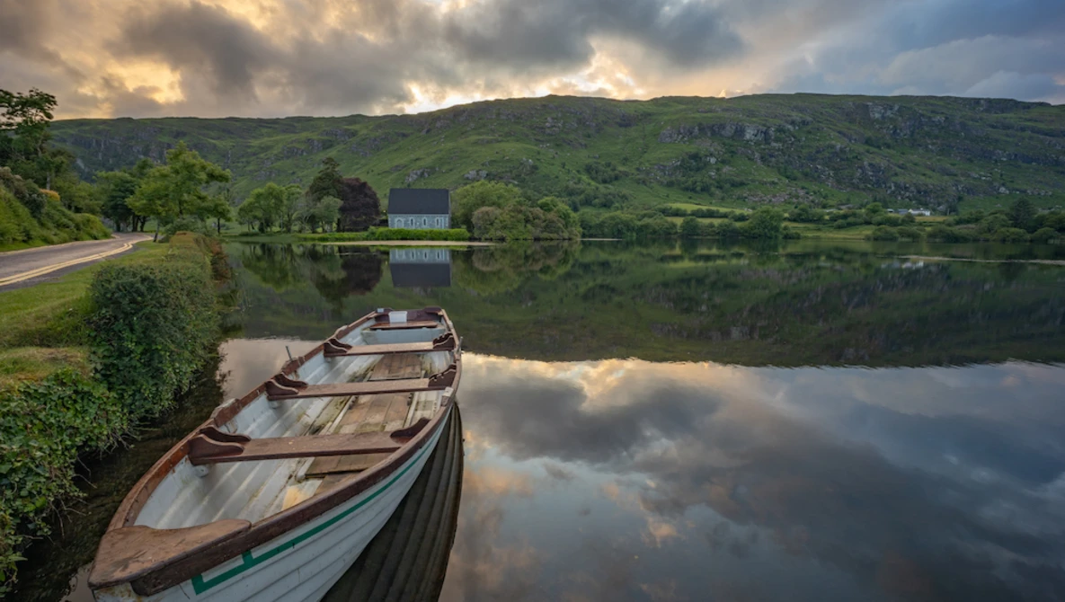 Wooden boats moored on still water with forested hills and dramatic sky reflected in the lake.