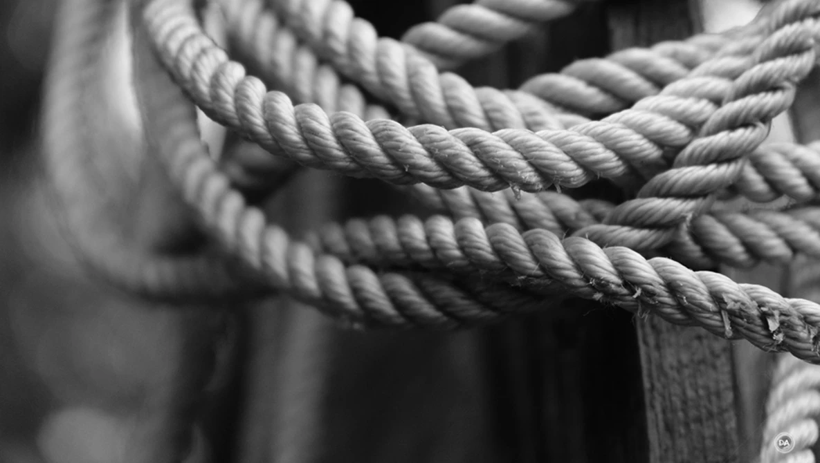Close-up of thick twisted rope coiled and layered, photographed in black and white with sharp detail and texture.