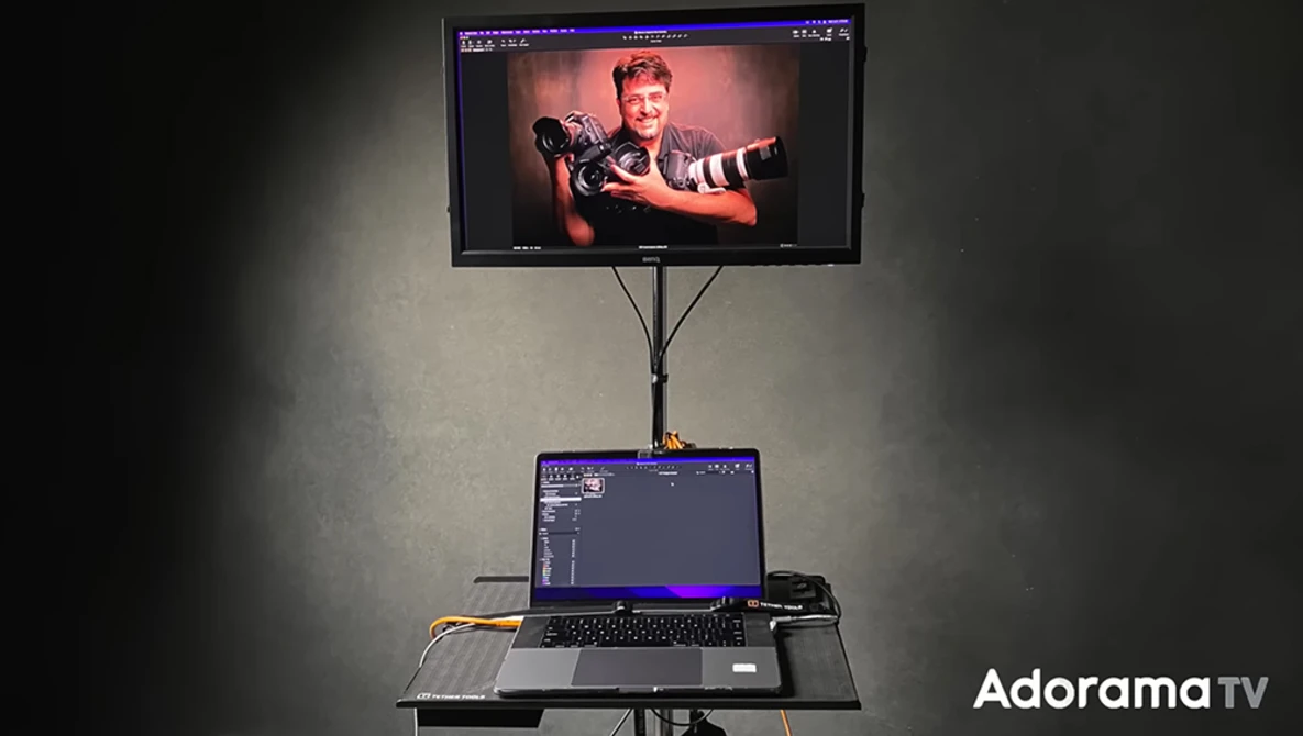 Monitor on adjustable stand displaying portrait of person with arms outstretched, laptop below showing editing interface.