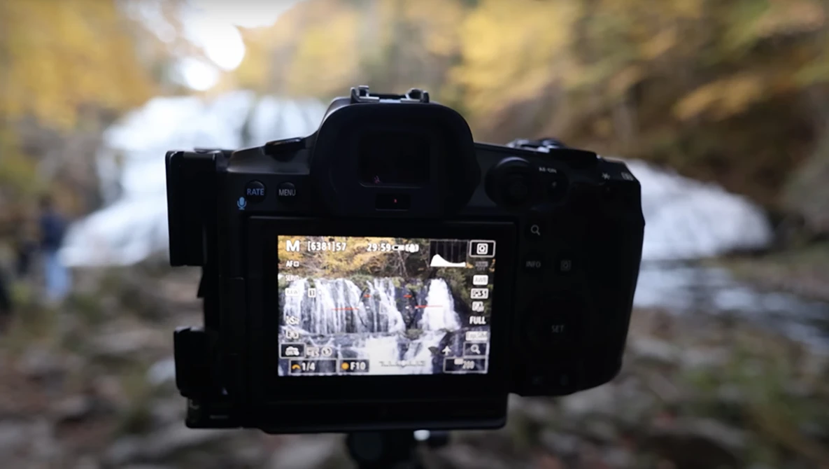 Camera on tripod displaying waterfall footage on LCD screen with blurred background.