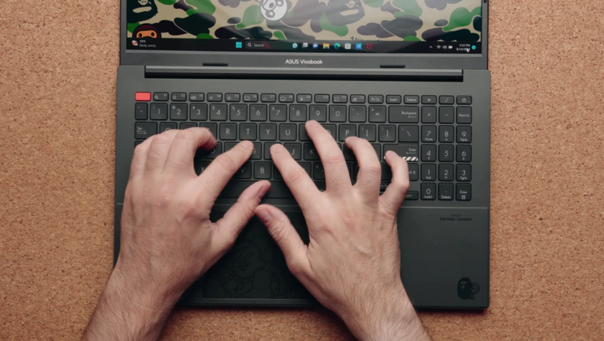 Overhead view of hands typing on an ASUS Vivobook laptop with camouflage pattern on screen.
