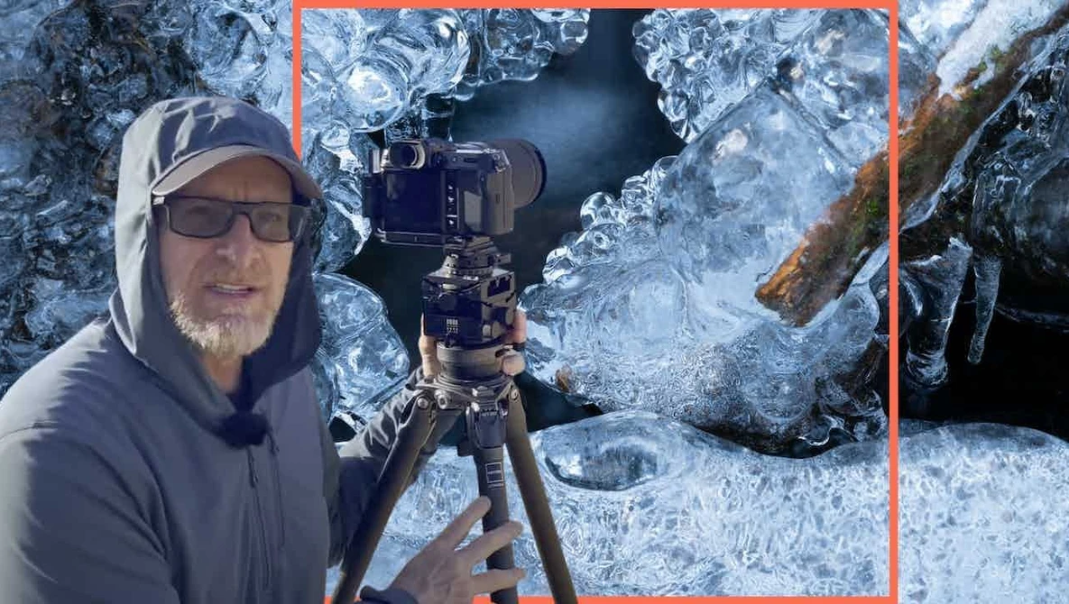 Photographer in winter gear holding a camera on a tripod amid ice-covered rocks and frozen surfaces.
