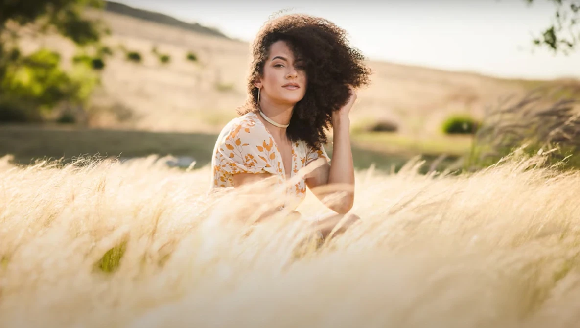 Woman with curly dark hair posing in a wheat field during golden hour.