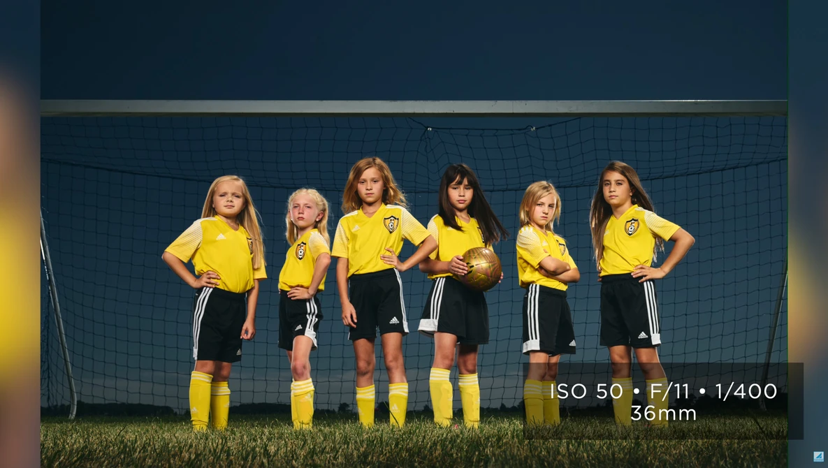 Six young soccer players in yellow jerseys and black shorts stand in a line in front of a goal net.