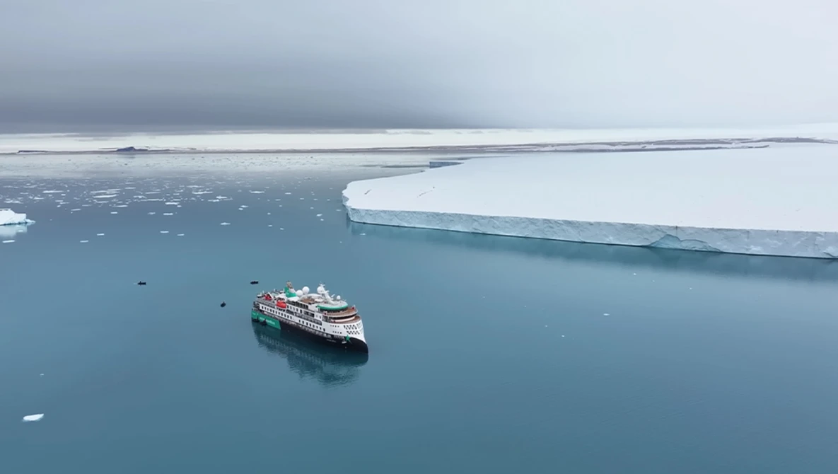 Expedition cruise ship navigating through icy Arctic waters surrounded by white ice floes and a massive ice shelf.