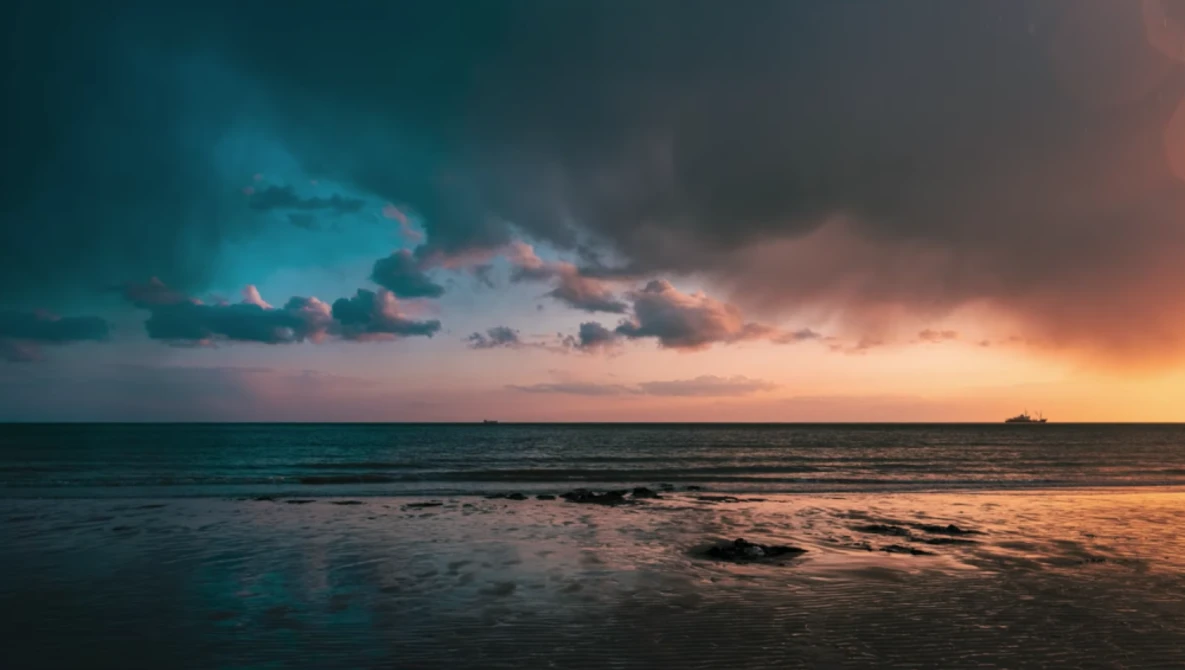 Dramatic sunset over calm ocean waters with layered storm clouds illuminated by golden and blue light.