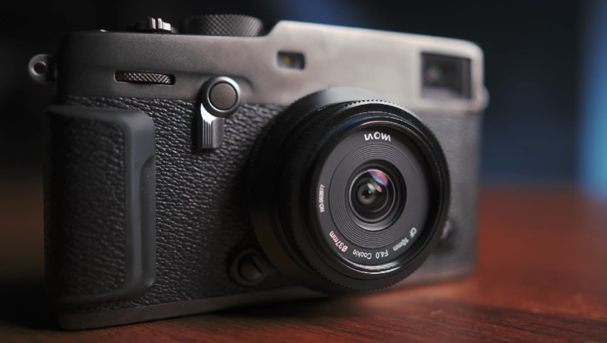 Instant film camera with black textured body and fixed lens on wooden surface.