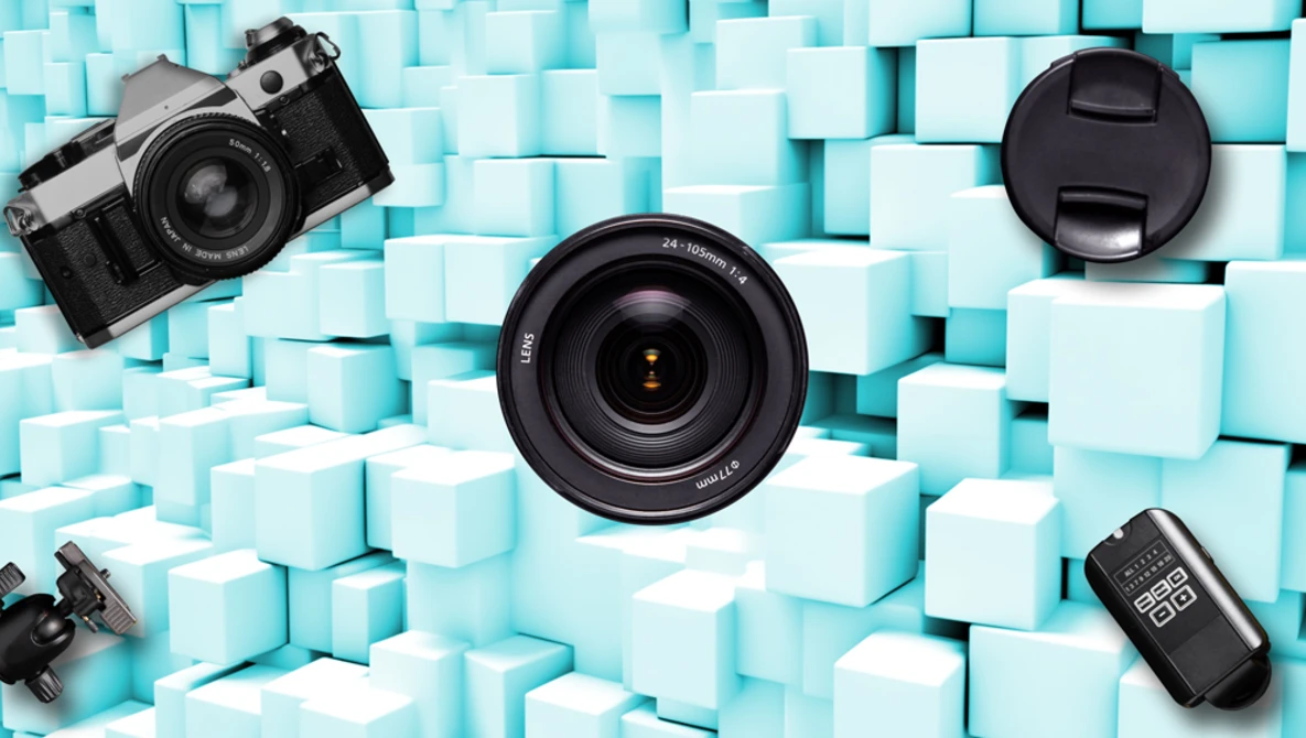 Camera lens and vintage film camera arranged on turquoise cubic blocks with a light meter visible.