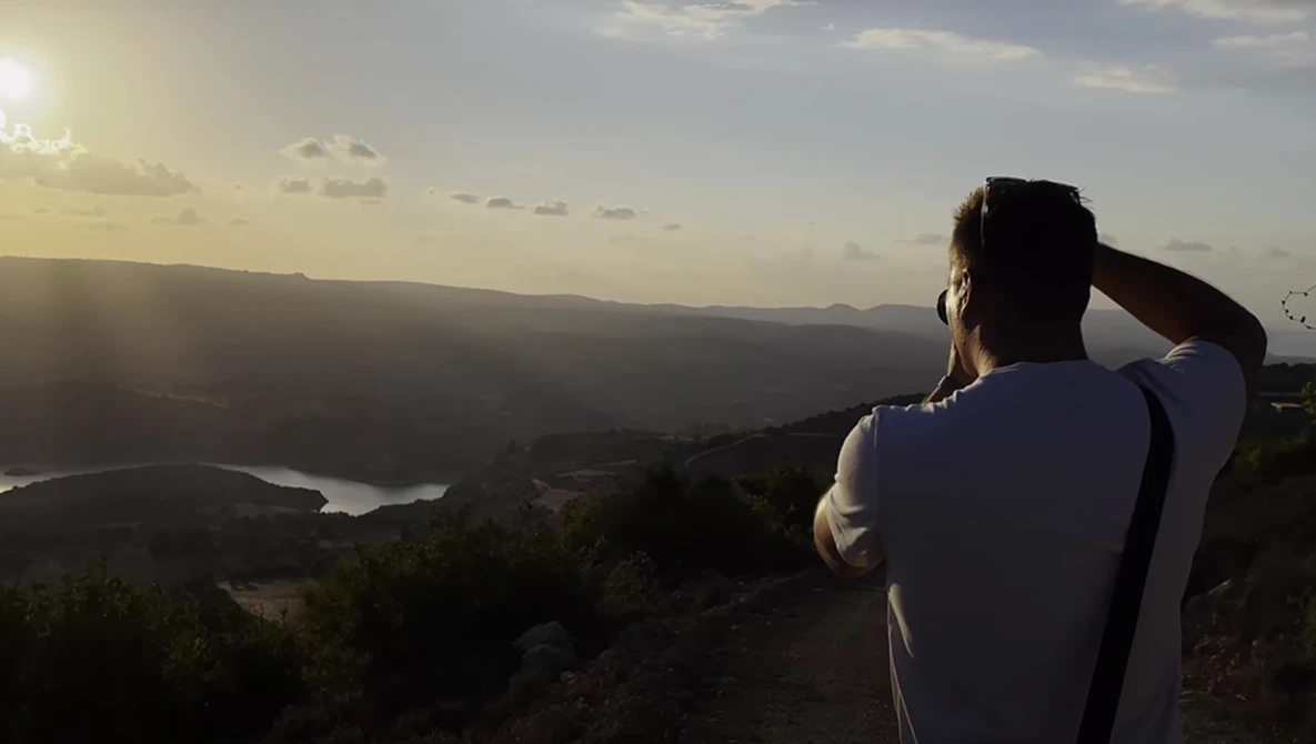 Photographer silhouetted against a vast landscape with mountains and a winding river at golden hour.