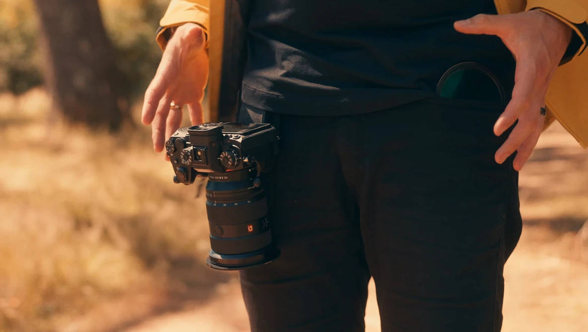 Photographer holding a mirrorless camera with telephoto lens during golden hour outdoor shoot.