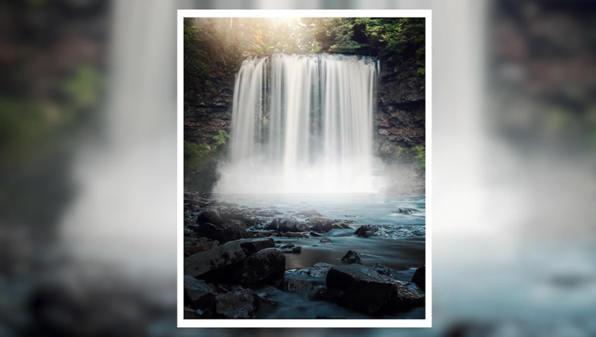 Waterfall cascading over dark rocky cliff with mist and turquoise pool below, surrounded by green forest.