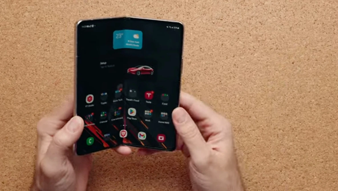 Hands holding a foldable smartphone with dark interface displaying app icons and a red car image.