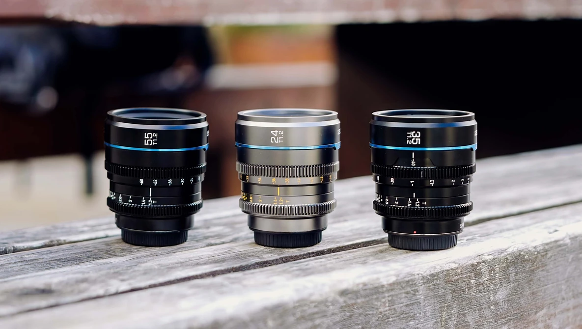 Three vintage cinema lenses arranged in a row on a wooden surface, displaying blue, silver, and blue lens barrels with manual focus rings.