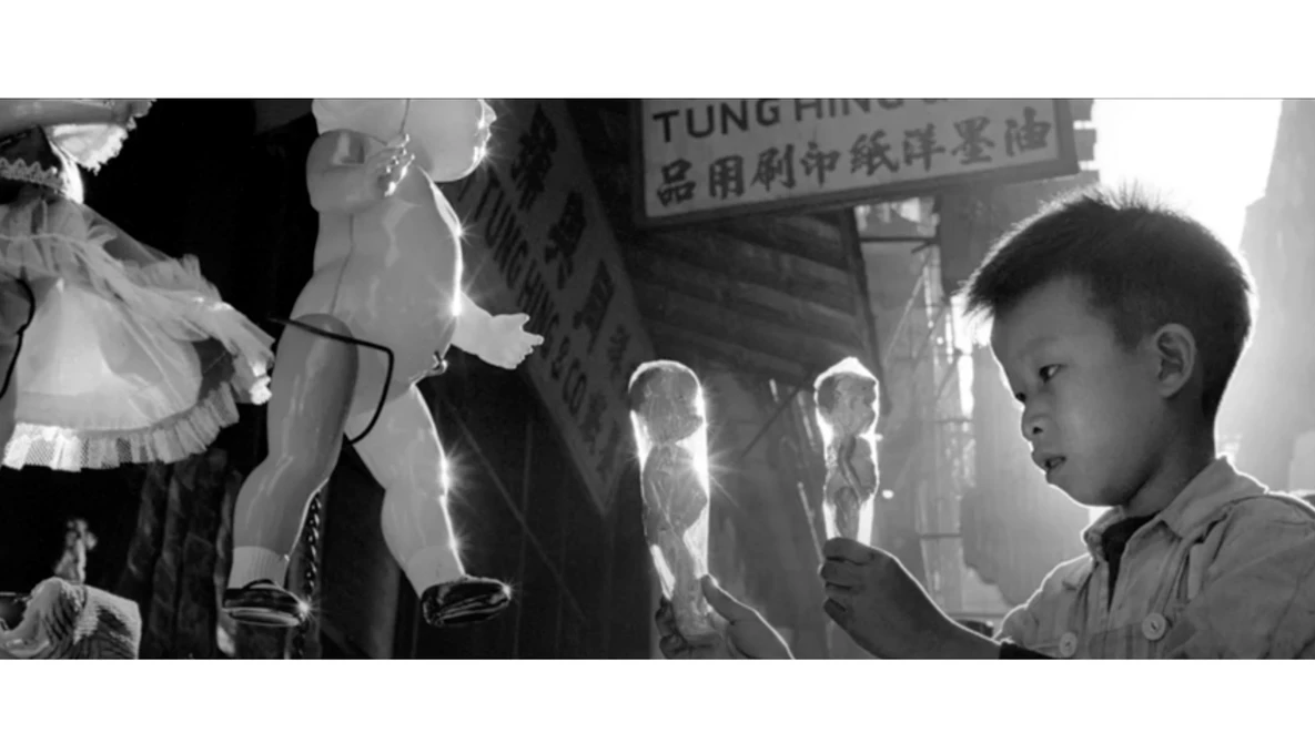 Young boy in profile looking at illuminated figures in a crowded urban street scene shot in black and white.
