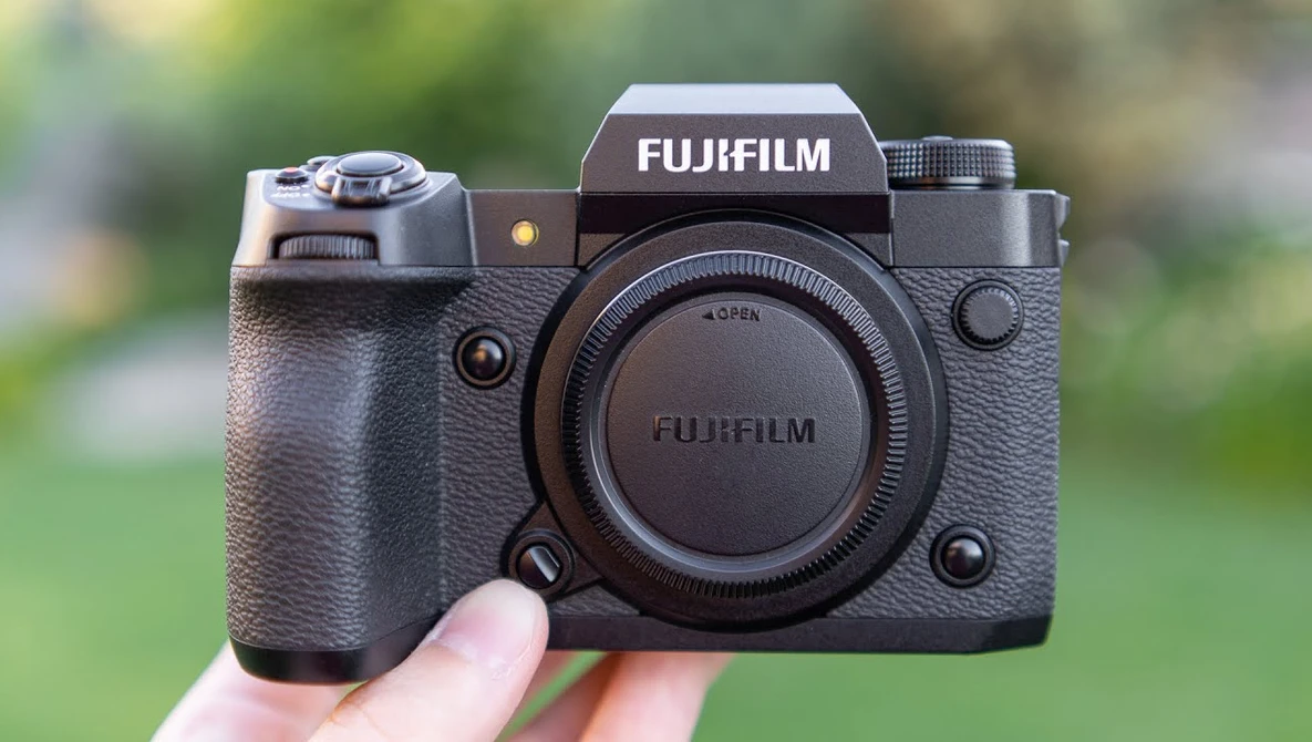 Fujifilm X-H2S mirrorless camera body held in hand against blurred green background.