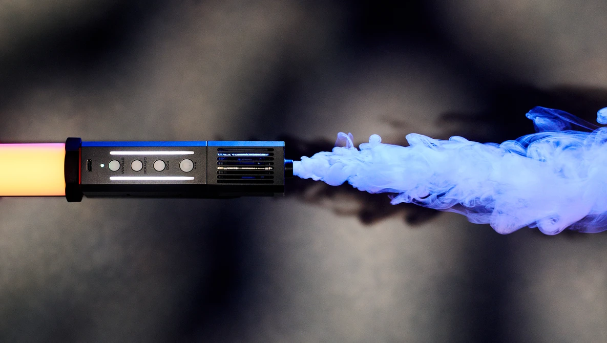 Yellow-gripped device emitting blue vapor against a dark blurred background.